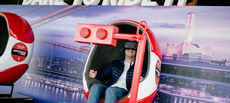 Someone fully immersed in a thrilling VR ride at A'DAM Lookout, located in A'DAM Tower, Amsterdam, experiencing a dynamic virtual reality adventure with stunning views of the city.